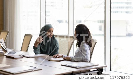 Serious young Arab manager woman talking to female business colleague Serious young Arab manager woman talking to female business colleague 117976263