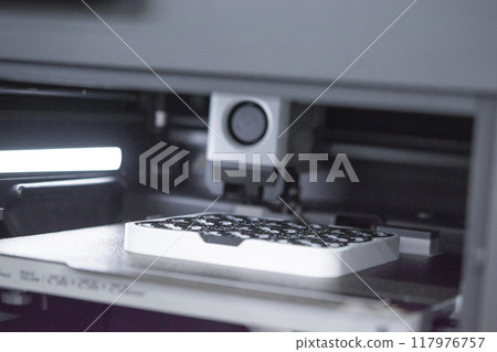 3D printer close up. A working 3D printer in process of printing object from molten plastic. 3D printer creating model by flowing liquid plastic from an extruder of printer. 3D printing technology 117976757