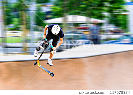 Young man practicing Scootering (Freestyle Scootering) in the new SkatePark in the central park of Igualada, Barcelona, Spain. blurred background 117978524