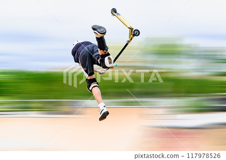 Young man practicing Scootering (Freestyle Scootering) in the new SkatePark in the central park of Igualada, Barcelona, Spain. blurred background 117978526