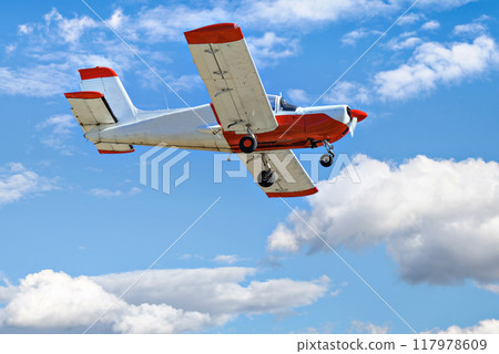 Single engine ultralight plane flying in the blue sky with white clouds 117978609