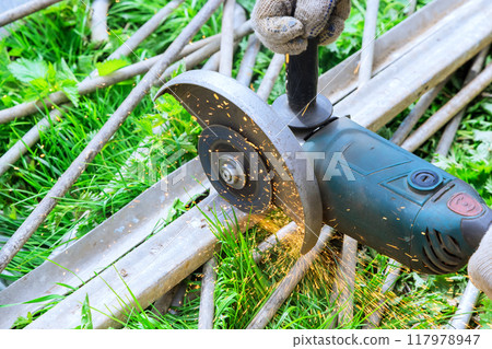 Worker uses an angle grinder hand saw to cut metal frames Worker uses an angle grinder hand saw to cut metal frames 117978947