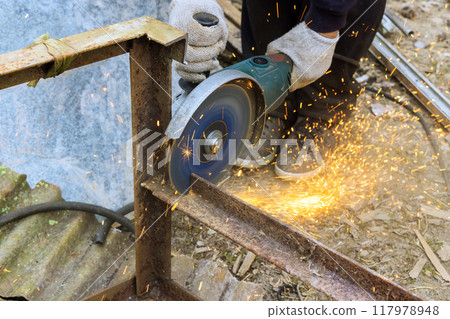 Worker uses an angle grinder hand saw to cut metal frame 117978948