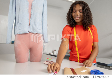 Smiling woman sewing fabric with needle at her tailoring workshop Smiling woman sewing fabric with needle at her tailoring workshop 117979006