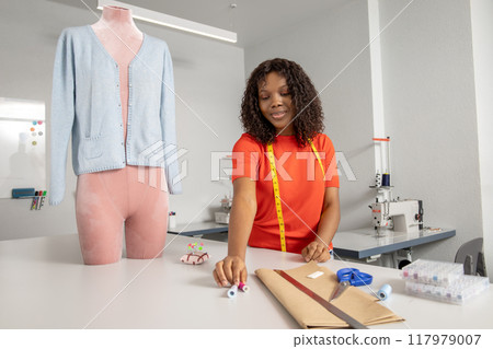 Female sewing fabric with needle at seamstress workplace 117979007