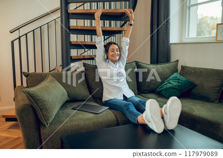 Woman in white shirt sitting on the sofa and stretching after a working day 117979089