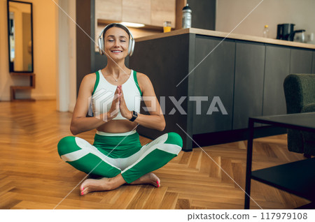 Smiling woman listening music while meditating in modern appartement Smiling woman listening music while meditating in modern appartement 117979108