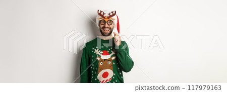 Christmas and holidays concept. Happy bearded man celebrating xmas, holding party mask and wearing Santa hat, smiling amazed, standing over white background Christmas and holidays concept. Happy bearded man celebrating xmas, holding party mask and wearing Santa hat, smiling amazed, standing over white background 117979163