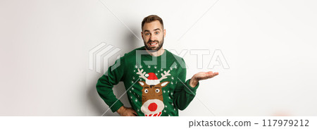 New Year, holidays and celebration. Confused bearded guy in funny sweater, shrugging and looking clueless, dont know, looking awkward, standing over white background 117979212