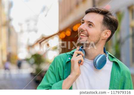 Portrait of smiling young male tourist in casual clothes with wireless headphones around neck 117979316