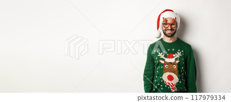Christmas holidays, celebration concept. Happy man in Santa hat and funny party glasses standing against white background Christmas holidays, celebration concept. Happy man in Santa hat and funny party glasses standing against white background 117979334