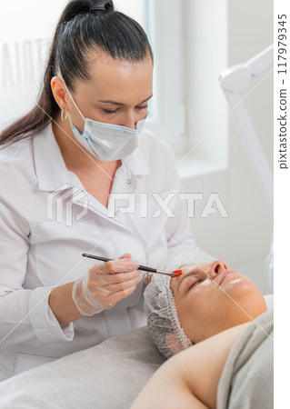 Beautician applying peeling moisturizing cream mask on young woman face for rehydrate face skin Beautician applying peeling moisturizing cream mask on young woman face for rehydrate face skin 117979345