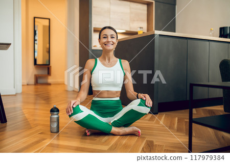 Sporty woman sitting in simple cross-legged position on floor 117979384