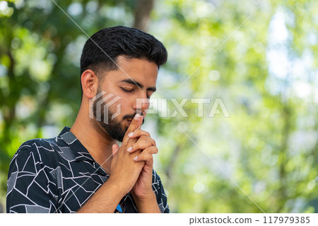 Indian man tourist praying with closed eyes to God asking for blessing, help, forgiveness outdoors 117979385