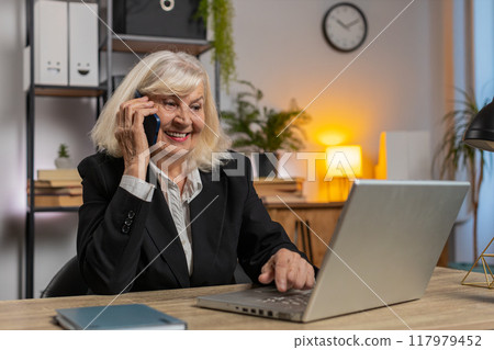 Senior Caucasian businesswoman operator using smartphone and laptop computer at home office desk 117979452