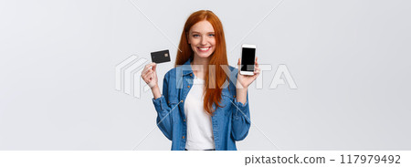 Waist-up portrait confident female with red long hair, blue eyes, holding credit card and showing smartphone display, easy banking service, payment for bills internet, smiling satisfied Waist-up portrait confident female with red long hair, blue eyes, holding credit card and showing smartphone display, easy banking service, payment for bills internet, smiling satisfied 117979492