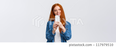 Waist-up portrait cheerful modern cute redhead woman taking photo of friend, smiling and tilt head lovely, looking mobile display, shooting beautiful scenery to post online in blog, white background Waist-up portrait cheerful modern cute redhead woman taking photo of friend, smiling and tilt head lovely, looking mobile display, shooting beautiful scenery to post online in blog, white background 117979510