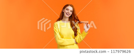 Carefree good-looking, smiling toothy redhead woman, girl with ginger hair laughing as chatting friends, rolling curl on hair, tilt head and smiling joyfully, having conversation, orange background 117979626