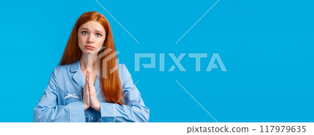 Please I am begging you. Silly and uneasy redhead caucasian girl in sleepwear, asking help, pleading forgiveness or need something, tilt head making sad face, standing blue background Please I am begging you. Silly and uneasy redhead caucasian girl in sleepwear, asking help, pleading forgiveness or need something, tilt head making sad face, standing blue background 117979635