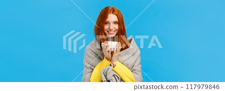 Winter holidays, people and emotions concept. Cheerful lovely and romantic redhead woman came home, warming with hot tea and smiling, wrap herself with grey scarf, standing blue background Winter holidays, people and emotions concept. Cheerful lovely and romantic redhead woman came home, warming with hot tea and smiling, wrap herself with grey scarf, standing blue background 117979846