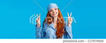 Silly and cute young redhead caucasian girl in sleep mask and nightwear, wearing lovely pyjama feeling alright, showing peace gestures and smiling, ready for sweet dreams, blue background Silly and cute young redhead caucasian girl in sleep mask and nightwear, wearing lovely pyjama feeling alright, showing peace gestures and smiling, ready for sweet dreams, blue background 117979880