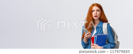 Uneasy and sad gloomy cute redhead female looking troubled camera, reading something worrying on smartphone display, holding mobile, backpack and notebooks as in university 117979885