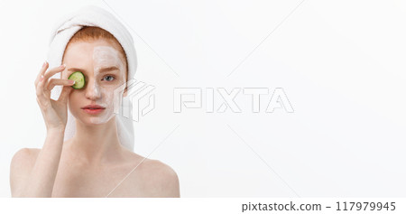Attractive Young Woman with beautiful clean skin. White mask and cucumbers. Beauty treatments and cosmetology spa therapy. White background 117979945