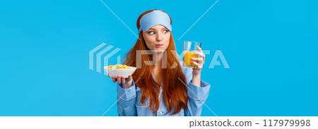Carefree good-looking caucasian pretty foxy girl, college student smiling amused staring at orange juice glass, holding cereals, eating morning meal, breakfast, standing blue background 117979998