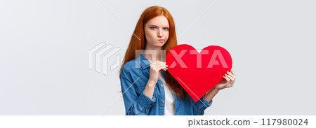 Serious-looking troubled, unsure cute redhead girl thinking what gift buy in addition to valentines day big red heart card, plan romantic date, pouting and frowning camera perplexed 117980024