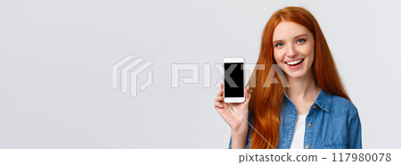 Close-up portrait modern millennial cute redhead female with blue eyes, advice get cool new app, showing smartphone display and smiling, advertising game or photo filter application 117980078