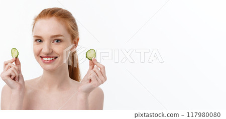 Close up beauty portrait of a smiling beautiful half naked woman holding cucumber slices at her face isolated over white background Close up beauty portrait of a smiling beautiful half naked woman holding cucumber slices at her face isolated over white background 117980080