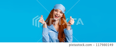Cheerful and cute, lovely redhead caucasian girl in nightwear, sleep mask, tilt head and smiling, showing korean heart, love sign and standing blue background upbeat, feeling well rested Cheerful and cute, lovely redhead caucasian girl in nightwear, sleep mask, tilt head and smiling, showing korean heart, love sign and standing blue background upbeat, feeling well rested 117980149