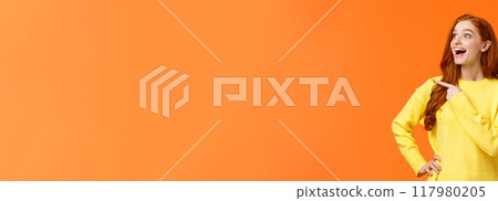 Look at that, wow. Impressed and fascinated, astonished cute redhead woman stare and pointing left with excited, happy smile, shoppaholic adore winter holiday sales, express interest and admiration 117980205