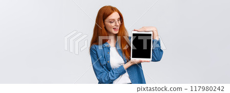 Technology and people concept. Attractive creative young redhead girl creating design project for university, holding digital tablet and introduce something on device screen, white background Technology and people concept. Attractive creative young redhead girl creating design project for university, holding digital tablet and introduce something on device screen, white background 117980242