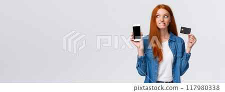 Shopaholic cant hold herself want buy something online. Eager and excited redhead girl see tempting price internet store, biting lip thrilled stare smartphone display, hold credit card Shopaholic cant hold herself want buy something online. Eager and excited redhead girl see tempting price internet store, biting lip thrilled stare smartphone display, hold credit card 117980338