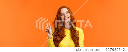 Waist-up cheerful gorgeous redhead woman with long curly red hair, showing peace sign and smiling happily, express positivity, like winter holidays, standing orange background Waist-up cheerful gorgeous redhead woman with long curly red hair, showing peace sign and smiling happily, express positivity, like winter holidays, standing orange background 117980342