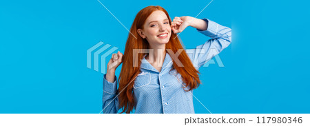 Tender sleepy redhead teenage girl stretching with hands raised, smiling satisfied, had great sleep, waking up and grinning delighted, waiting for morning coffee, wearing pyjama, blue background Tender sleepy redhead teenage girl stretching with hands raised, smiling satisfied, had great sleep, waking up and grinning delighted, waiting for morning coffee, wearing pyjama, blue background 117980346