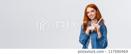 Good-looking charismatic dreamy redhead female in denim shirt, looking camera thoughtful and imaging, want draw something, have design project in mind, holding colored pencils, white background 117980469
