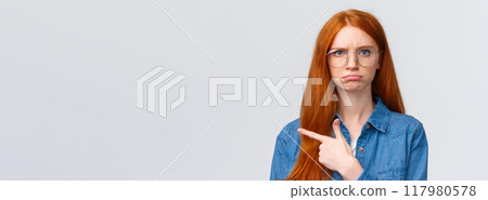 Close-up gloomy and upset, offended sulking girlfriend want something and pointing envy left, indicate disappointing promo, unfair situation, pouting and frowning look displeased, white background 117980578