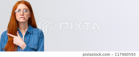 Nervousness, people and education concept. Anxious timid and insecure cute redhead girl in glasses, student worrying biting lip, hesitating telling something, pointing finger left, white background 117980593