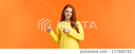 Time to prepare for holidays. Cheeky gorgeous smiling girl with red curly hair, pointing right, advice what shop visit, recommend online store for winter goods, standing orange background Time to prepare for holidays. Cheeky gorgeous smiling girl with red curly hair, pointing right, advice what shop visit, recommend online store for winter goods, standing orange background 117980782