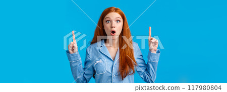 Wow look at this discounts. Amazed and surprised, excited young redhead woman in nightwear telling about stunning unexpected news, pointing fingers up, folding lips and stare astonished 117980804