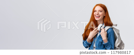 Education, student life and happiness concept. Cheerful good-looking redhead caucasian girl, college student with backpack and headphones over neck laughing smiling at camera Education, student life and happiness concept. Cheerful good-looking redhead caucasian girl, college student with backpack and headphones over neck laughing smiling at camera 117980817