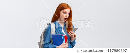 Awesome no classes today. Amazed and excited redhead teenage girl gasping as reading cool message on smartphone, holding backpack notebooks and mobile phone, white background 117980897