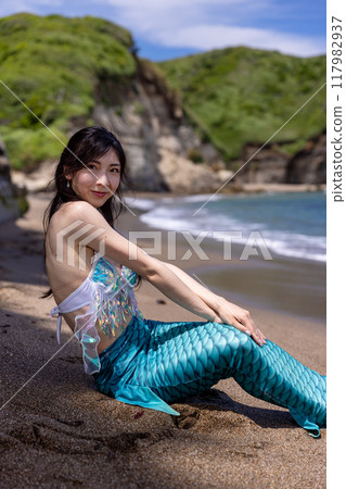 年輕的女美人魚坐在夏日海邊的沙灘上微笑 117982937