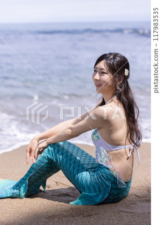年輕的女美人魚坐在海邊的沙灘上 117983535