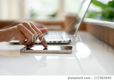 A close-up image of a woman's finger touching on a smartphone screen on a table. A close-up image of a woman's finger touching on a smartphone screen on a table. 117983640