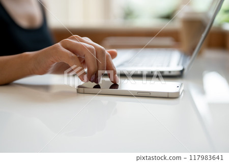 A close-up image of a woman's finger touching on a smartphone screen on a table. 117983641