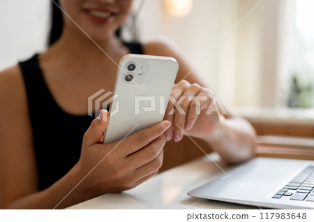 A woman working remotely from a coffee shop, checking reading messages on her smartphone. 117983648