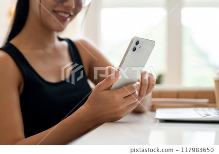 A woman working remotely from a coffee shop, checking reading messages on her smartphone. A woman working remotely from a coffee shop, checking reading messages on her smartphone. 117983650